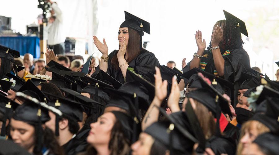 2 female graduates giving a standing ovation to the commencement speaker